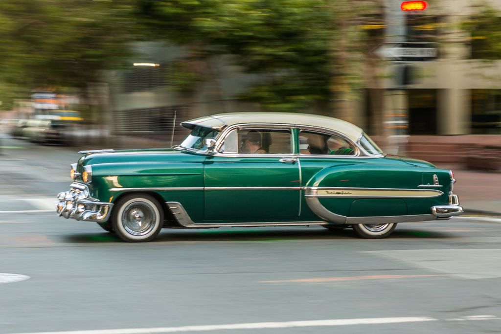 Classic vintage car in motion on a busy city street, exemplifying speed and style.